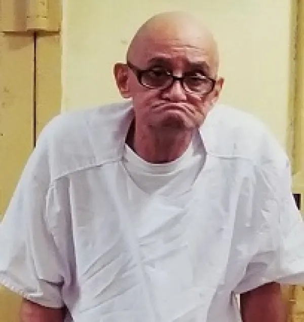 Bald old man with black-rimmed glasses and ears sticking out on each side of his had big a huge frown as if he has not teeth in a white hospital gown looking very sad