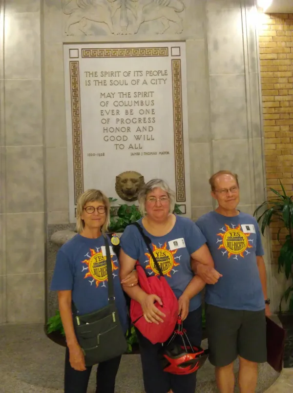 Three people standing in front of etched sign on wall