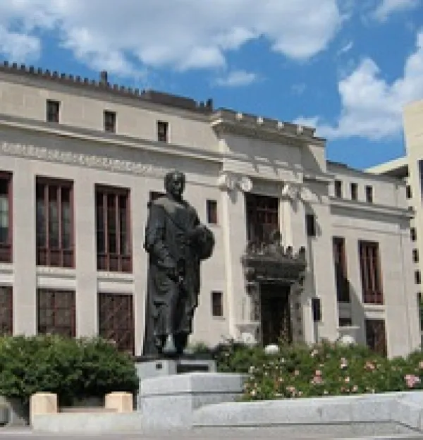 Big governmental building with statue of Christopher Columbus in front, some bushes against a blue sky with white clouds