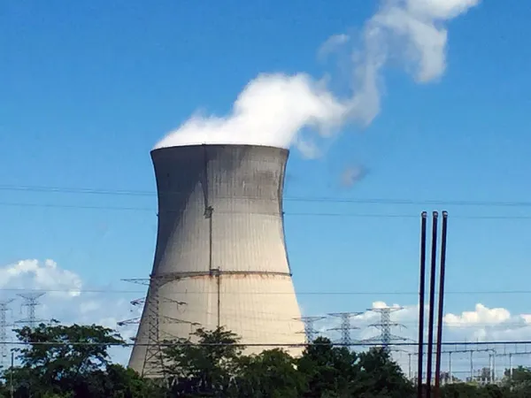 Nuclear tower with lots of white smoke coming out against a blue sky