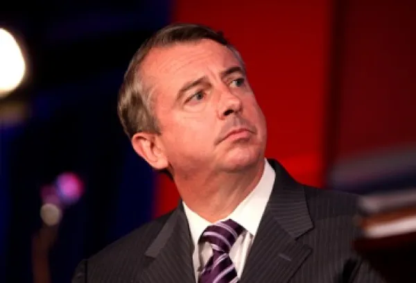 Middle aged white guy with receding brown hair looking sideways with a worried look on his face, wearing a gray suit with a purple and white striped tie