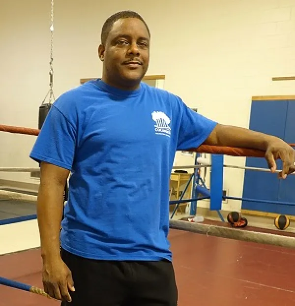 Black man in blue t-shirt standing next to a boxing ring
