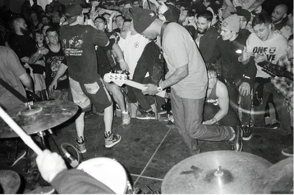 Black and white photo of black guy playing guitar with people all around dancing