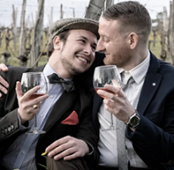 Two white guys one in a beret drinking wine and cuddling outside