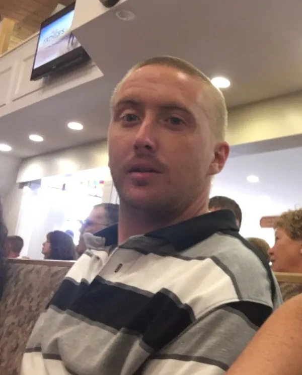 Man in his 20s with a bald head looking at the camera wearing a gray, white and black striped shirt