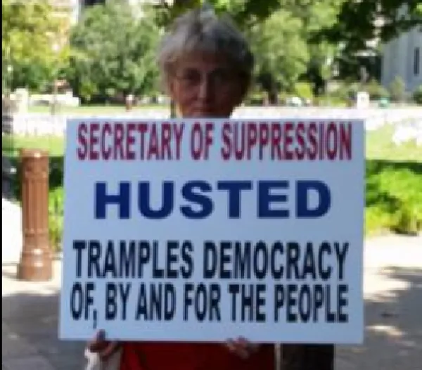 Woman holding sign against Jon Husted