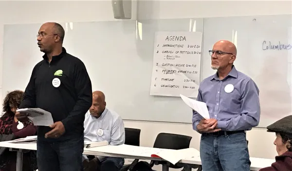 Two men at the front of a room speaking