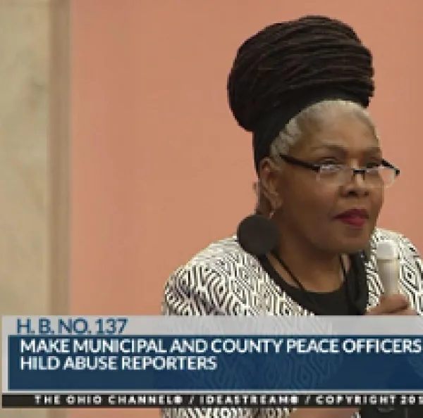 Black woman in glasses with hair rolled up on top of head with pink background and words at the bottom 