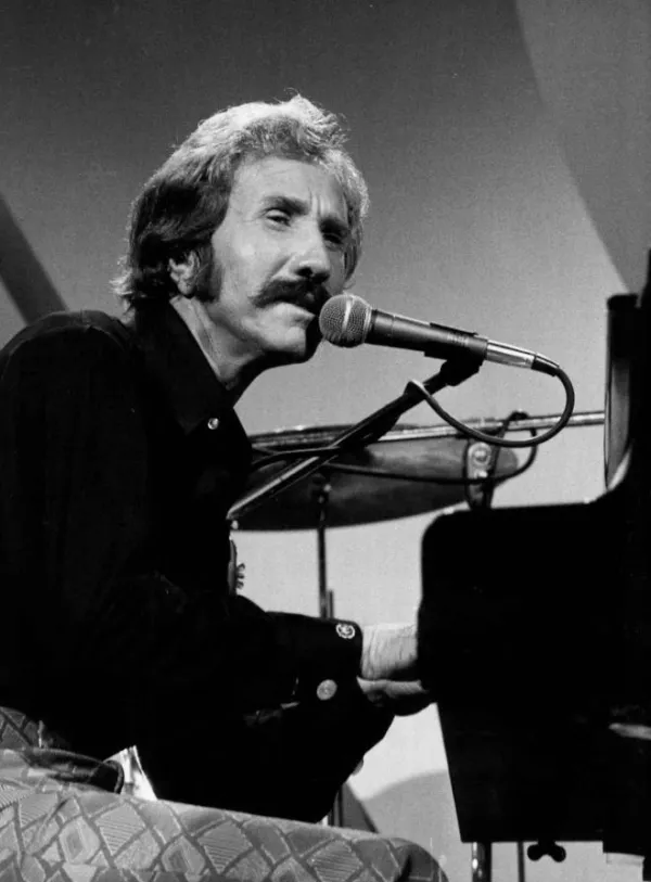 Black and white photo of guy with big mustache sitting at piano singing