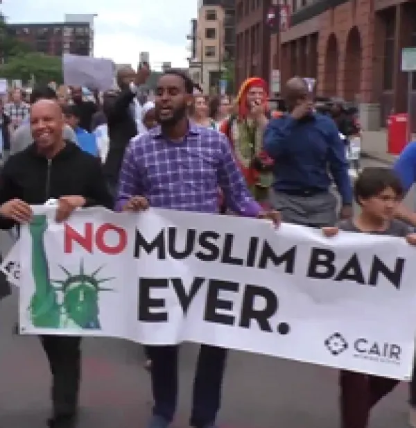 People marching outside with sign saying No Muslim Ban Even