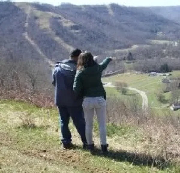 Backs of two people standing outside on a hill pointing off to the distance down in a valley