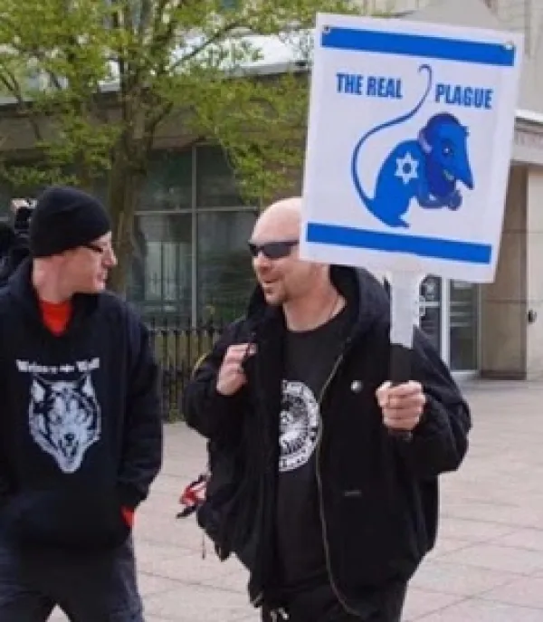 Protester outside Ohio statehouse with sign saying The Real Plague with a rat with a swatiska on it