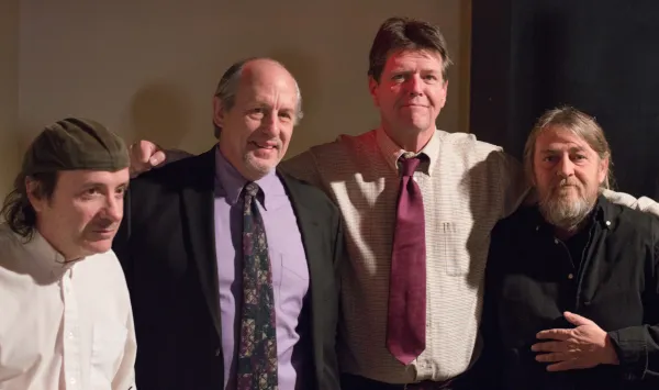 Four middle aged white guys, some in suits, standing together with their arms around each other