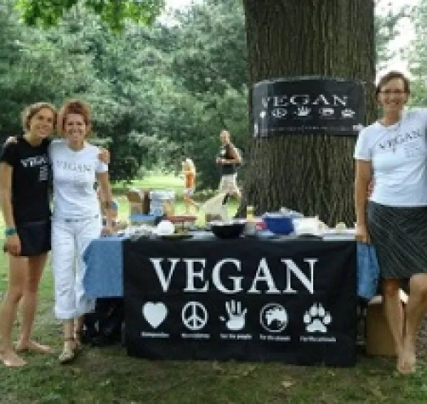 Three happy people by a table outside that says VEGAN on a sign