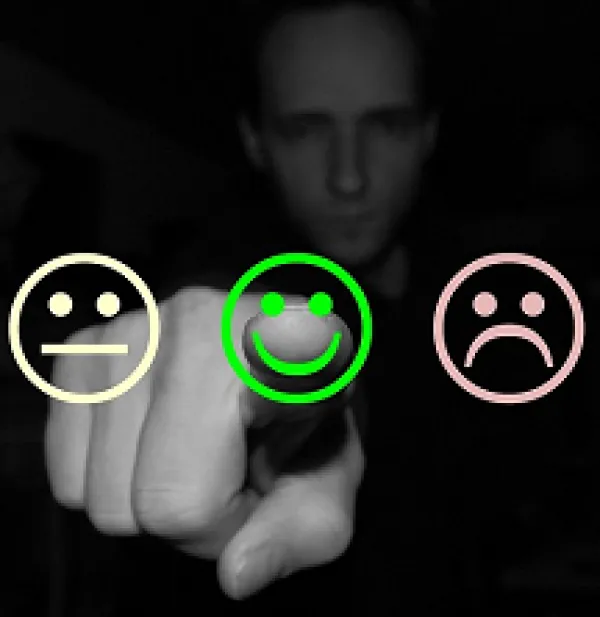 A black and white man in the background pointing his finger to the camera with a straight line face, happy face and sad face drawn on front