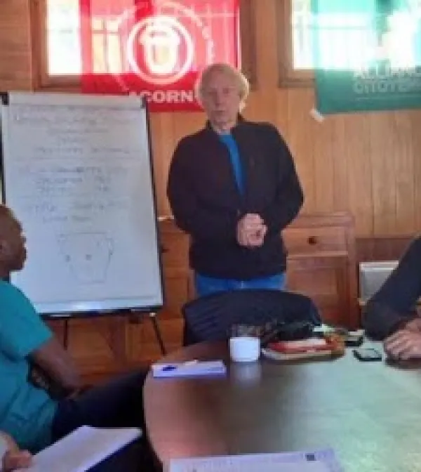 Gray haired thin man standing by a white paper flip chart in front of a group of people at a table