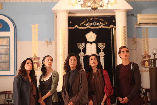 Four women staring up at something above them, standing in front of an elaborately decorated doorway