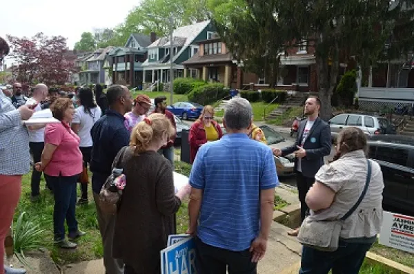 A group with a variety of black and white, old and young people standing outside in a neighborhood with trees and houses