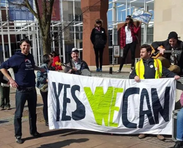 People holding a Yes We Can sign outside a brick building