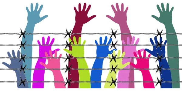 Different color arms and hands reaching up behind a barbed wire fence