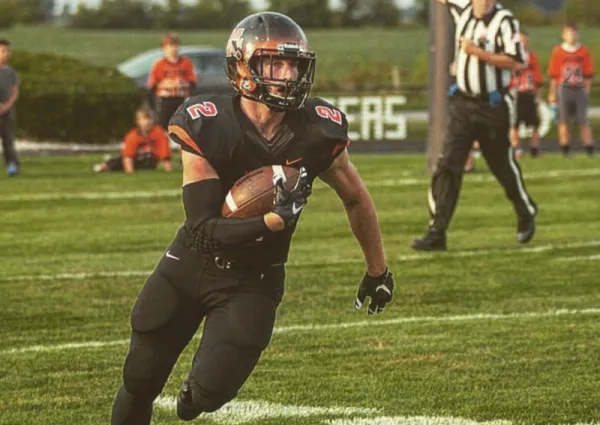 Football player running with the ball in his arm in brown and orange uniform